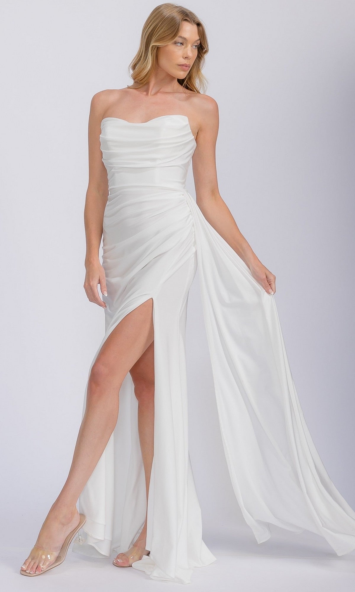 A woman wears the Eureka EK178 Long Prom Dress, a white strapless gown with a high slit and sheer overlay, standing against a plain light background.